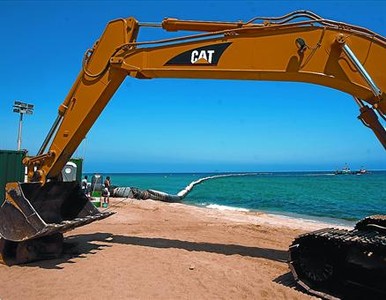 Una excavadora espera a la platja de Cabrera la sorra enviada pel vaixell draga (al fons), al juliol.