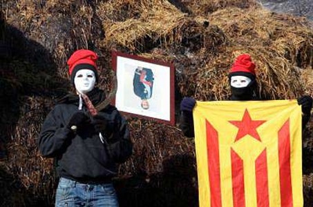 Dos joves amb barretina flanquegen el retrat segrestat de cap per avall del Rei.