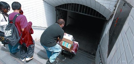 Un home carregat amb caixes baixa penosament per les escales del metro d'Arc de Triomf.